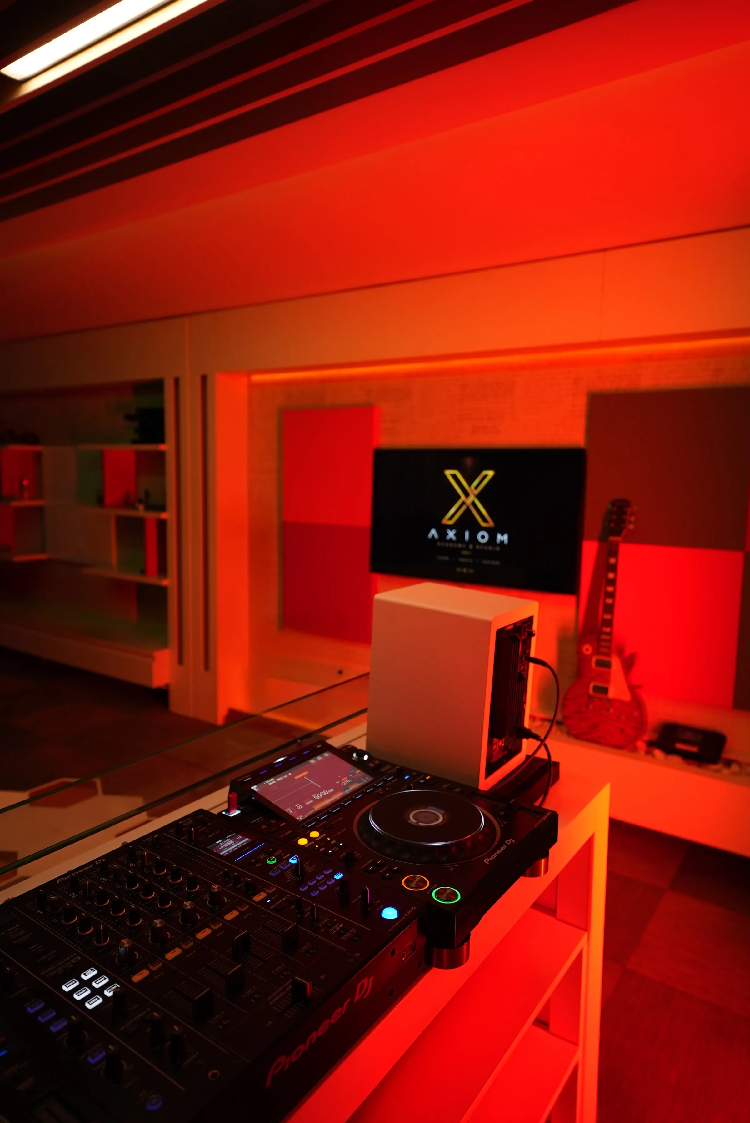 Kırmızı ışıklarla aydınlatılmış AXIOM stüdyosundaki DJ ekipmanı.
